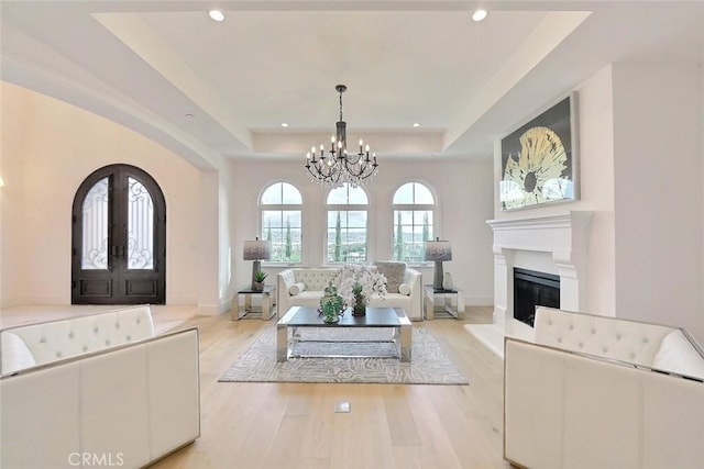 living room featuring a raised ceiling, french doors, an inviting chandelier, and light hardwood / wood-style flooring