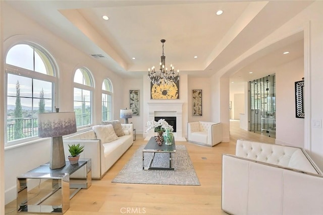 living room with light wood-type flooring, a tray ceiling, and a chandelier