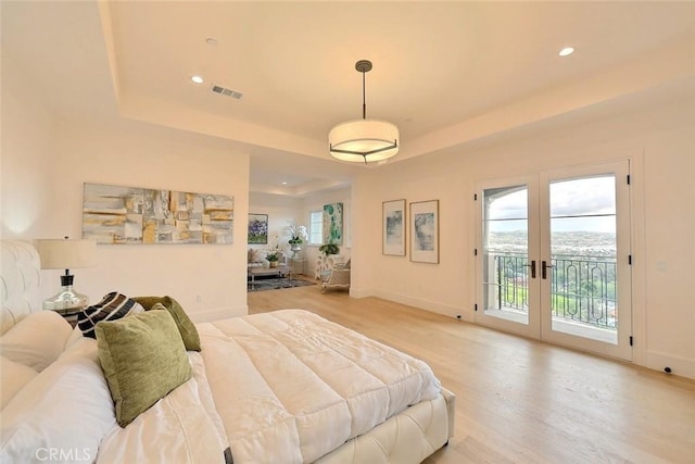 bedroom featuring a raised ceiling, french doors, access to outside, and light hardwood / wood-style flooring