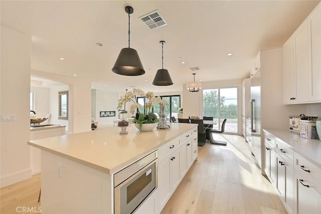 kitchen with hanging light fixtures, light hardwood / wood-style flooring, white cabinets, a center island, and stainless steel microwave