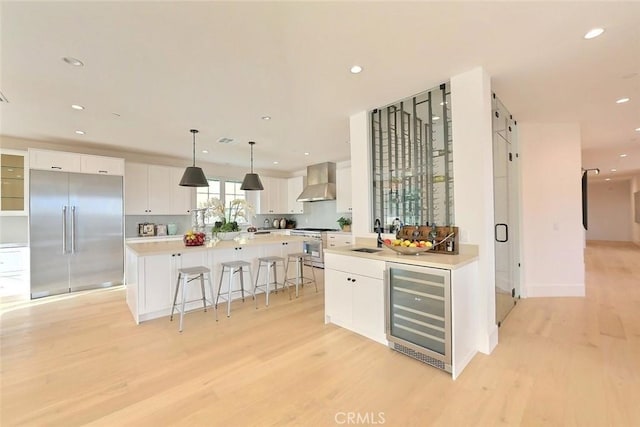 kitchen featuring a center island, wall chimney exhaust hood, wine cooler, high quality appliances, and white cabinets