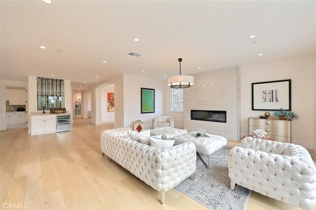 living room featuring a large fireplace, light wood-type flooring, and beverage cooler