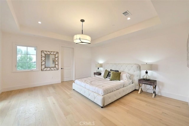 bedroom with light hardwood / wood-style floors and a tray ceiling