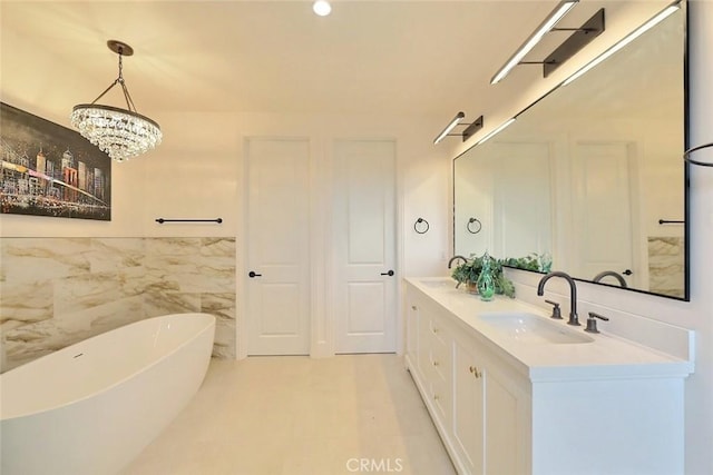 bathroom with a tub, vanity, a chandelier, and tile walls