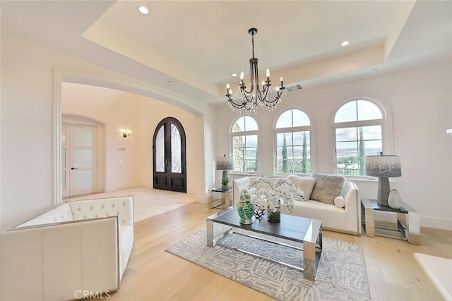 living room with a raised ceiling, french doors, light hardwood / wood-style floors, and an inviting chandelier