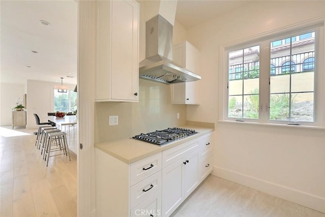 kitchen with white cabinetry, a healthy amount of sunlight, wall chimney range hood, and stainless steel gas stovetop