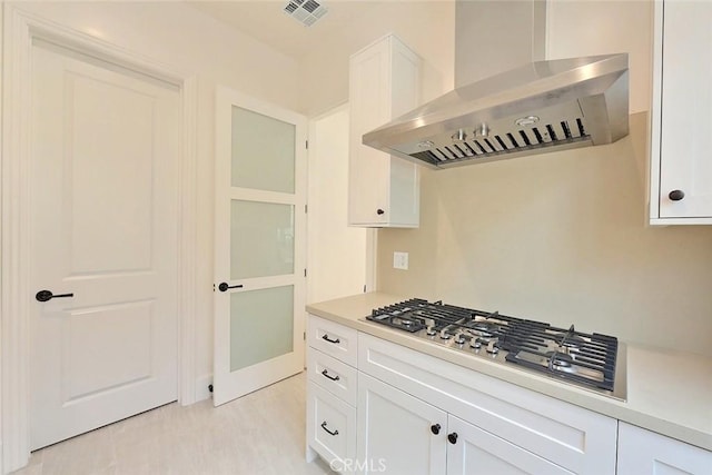 kitchen with white cabinets, light hardwood / wood-style floors, wall chimney range hood, and stainless steel gas stovetop