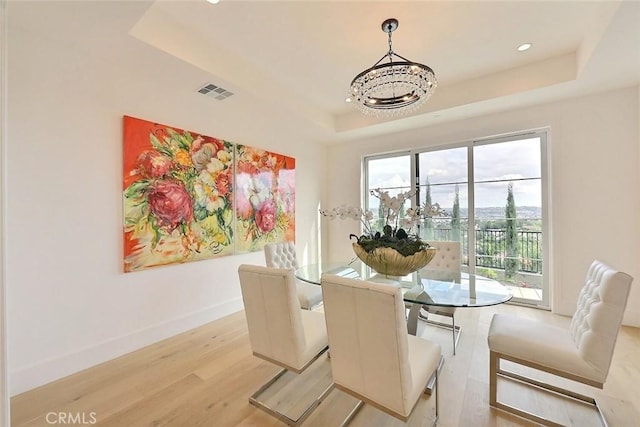 dining space with a raised ceiling, light hardwood / wood-style flooring, and a notable chandelier