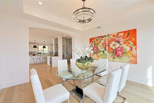 dining room featuring a raised ceiling, light hardwood / wood-style floors, and a notable chandelier