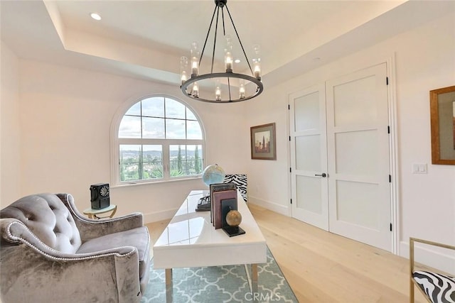 living area featuring a raised ceiling, light hardwood / wood-style flooring, and an inviting chandelier