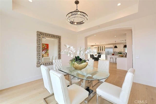 dining room with a notable chandelier, a raised ceiling, and light wood-type flooring