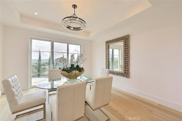 dining space featuring a tray ceiling, light hardwood / wood-style floors, and a notable chandelier