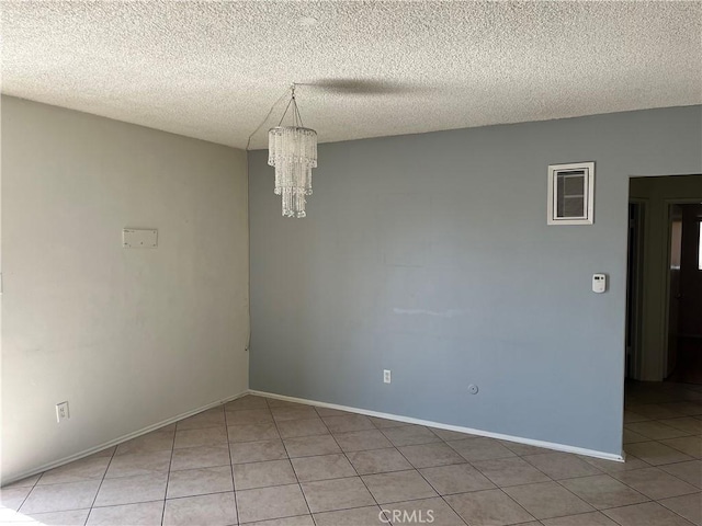 tiled spare room featuring a chandelier and a textured ceiling