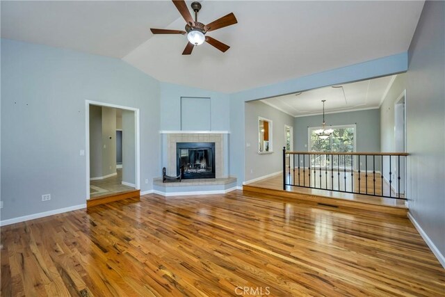 unfurnished living room with lofted ceiling, a tile fireplace, ceiling fan with notable chandelier, and hardwood / wood-style flooring