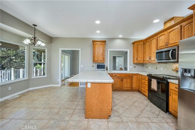 kitchen with kitchen peninsula, stainless steel appliances, decorative backsplash, a notable chandelier, and a kitchen island