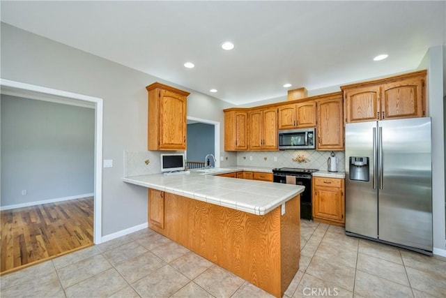 kitchen featuring appliances with stainless steel finishes, light tile patterned floors, kitchen peninsula, and backsplash