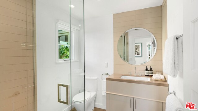 bathroom with toilet, a shower with shower door, vanity, tile walls, and tasteful backsplash