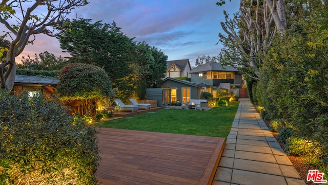 back house at dusk with a yard and a deck