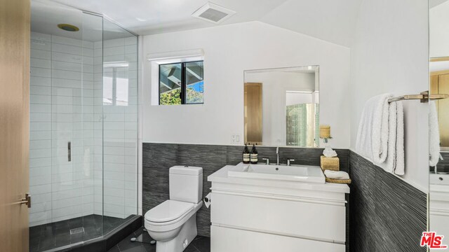 bathroom featuring vanity, toilet, tile walls, and a shower with shower door