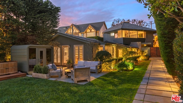 back house at dusk featuring a patio, an outdoor living space, french doors, and a yard