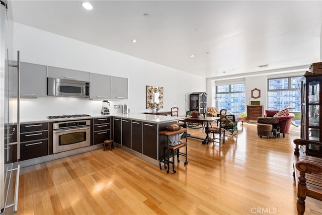 kitchen with appliances with stainless steel finishes, kitchen peninsula, and light wood-type flooring