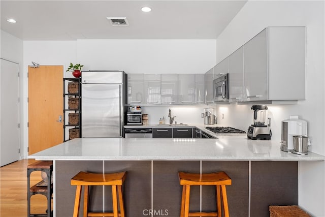 kitchen featuring sink, kitchen peninsula, light hardwood / wood-style floors, stainless steel appliances, and a breakfast bar