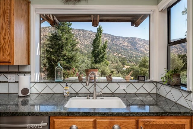 kitchen with a mountain view, backsplash, dark stone countertops, stainless steel dishwasher, and sink