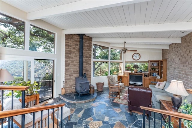 living room featuring ceiling fan, a wood stove, and beam ceiling