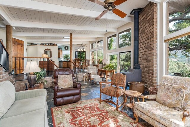 sunroom / solarium featuring beam ceiling, ceiling fan with notable chandelier, and a wood stove