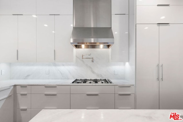 kitchen featuring stainless steel gas stovetop, white cabinetry, wall chimney range hood, and light stone counters