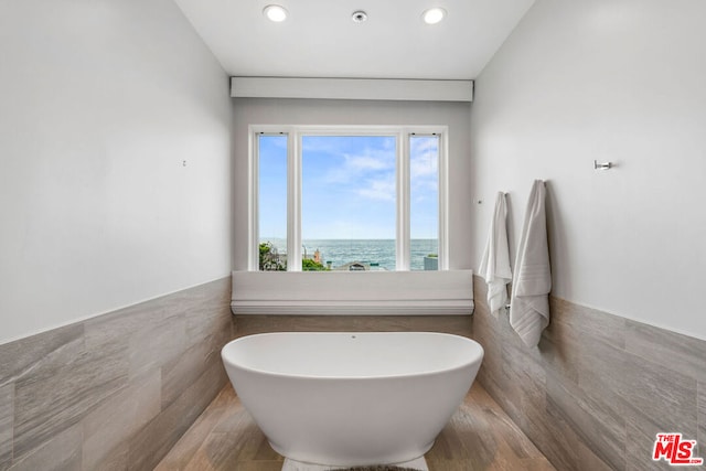 bathroom featuring tile walls, a water view, and a bathing tub