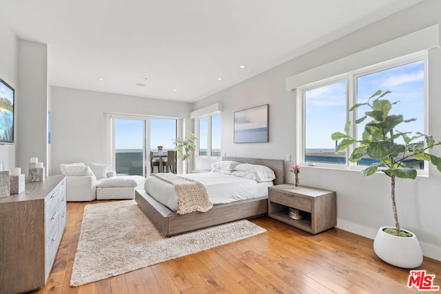 bedroom with light hardwood / wood-style flooring and a water view