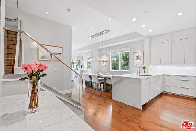 kitchen featuring white cabinets, kitchen peninsula, light stone countertops, hardwood / wood-style flooring, and sink