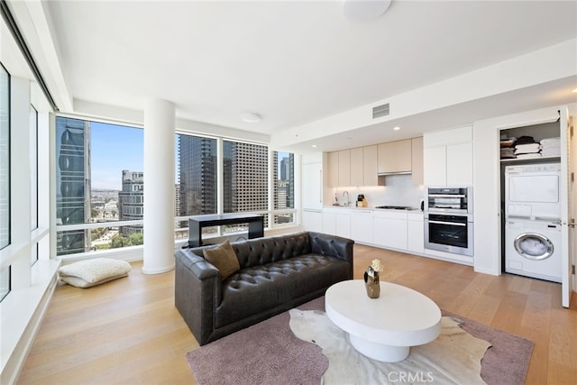 living room featuring stacked washing maching and dryer, light wood-style floors, a city view, visible vents, and recessed lighting