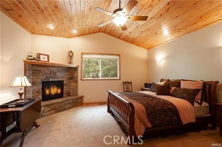 bedroom with wood ceiling, vaulted ceiling, ceiling fan, a fireplace, and carpet floors