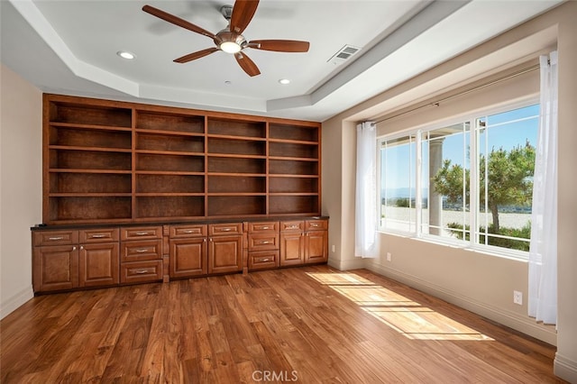 unfurnished office with wood-type flooring, a tray ceiling, and ceiling fan