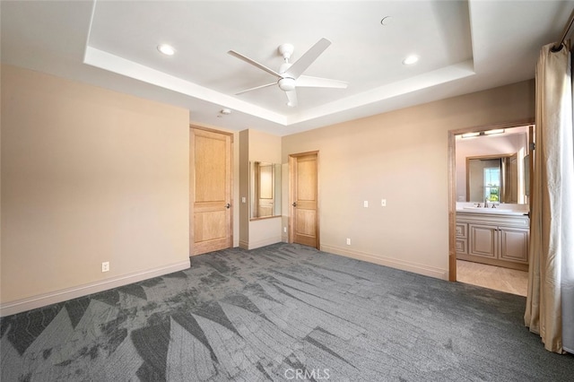 unfurnished bedroom featuring carpet floors, a tray ceiling, ceiling fan, ensuite bathroom, and sink