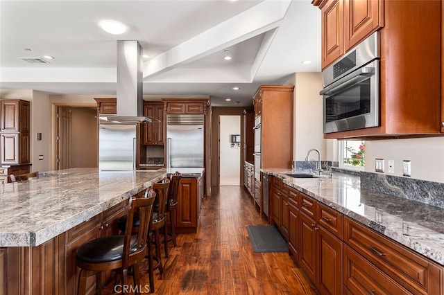 kitchen with a breakfast bar, dark wood-type flooring, sink, island exhaust hood, and appliances with stainless steel finishes