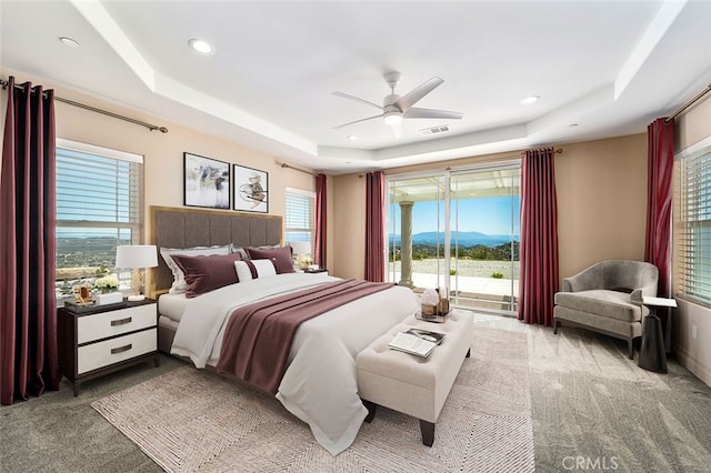 carpeted bedroom featuring ceiling fan, a tray ceiling, multiple windows, and access to outside