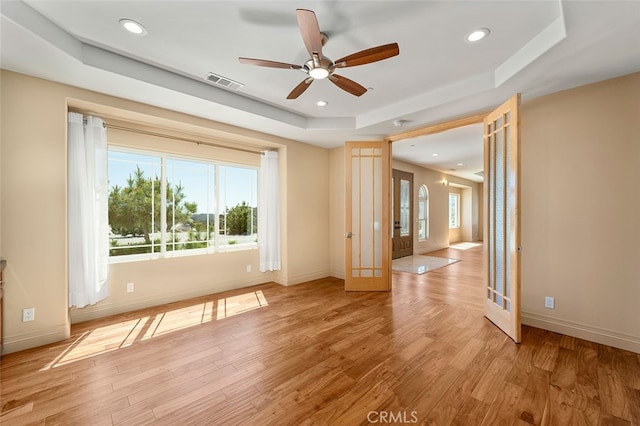 empty room featuring light hardwood / wood-style floors, a tray ceiling, and ceiling fan