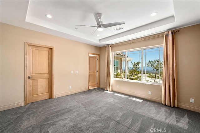 carpeted spare room with a tray ceiling and ceiling fan