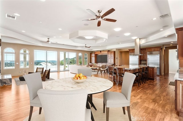 dining room with a raised ceiling, ceiling fan, and hardwood / wood-style flooring