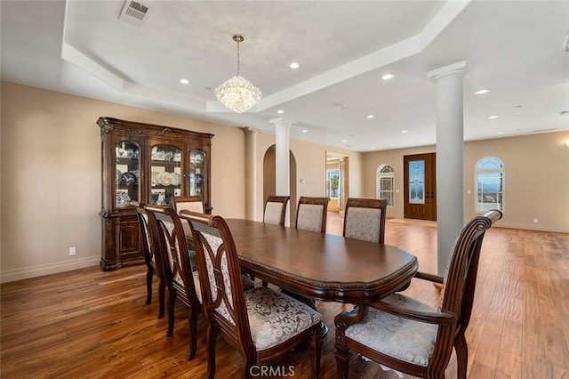 dining space featuring light hardwood / wood-style floors, a tray ceiling, a chandelier, and ornate columns