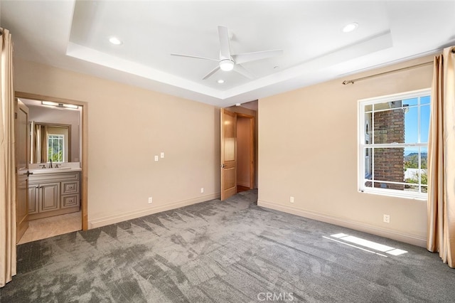 unfurnished bedroom with ceiling fan, a raised ceiling, ensuite bathroom, and carpet