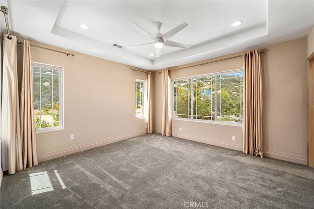 carpeted empty room featuring a tray ceiling, ceiling fan, and plenty of natural light