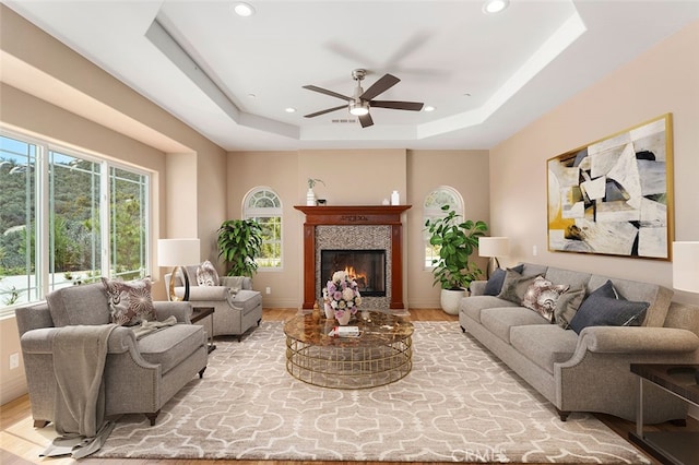 living room featuring a raised ceiling, ceiling fan, and light hardwood / wood-style flooring