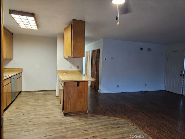 kitchen featuring light wood finished floors, light countertops, brown cabinetry, open floor plan, and dishwasher