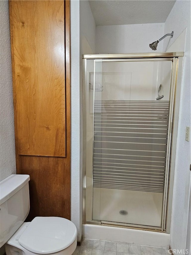 bathroom featuring toilet, a stall shower, and a textured wall