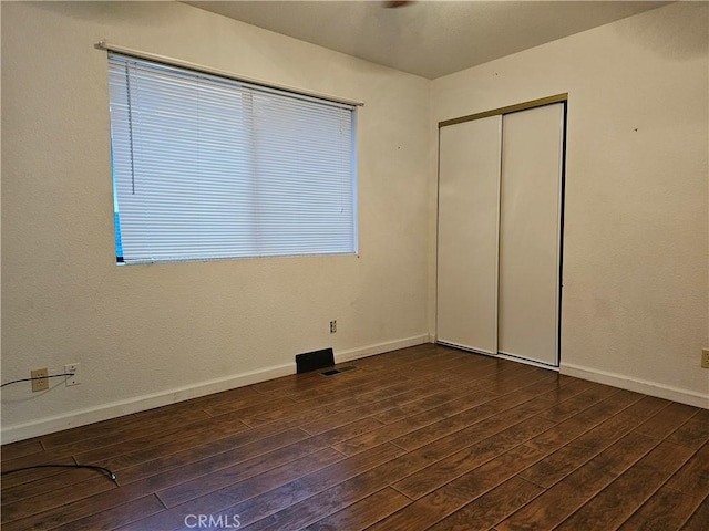 unfurnished bedroom with dark wood-type flooring, a closet, and baseboards