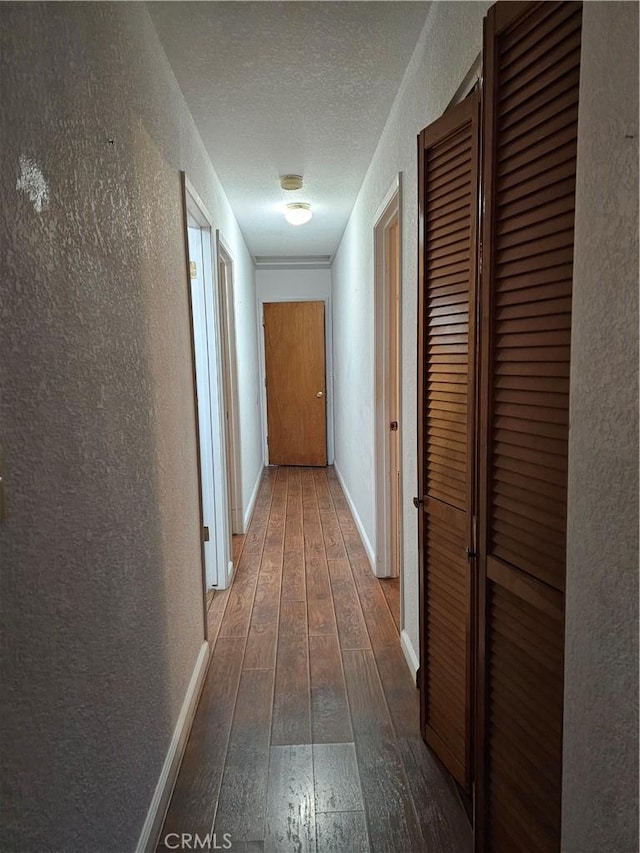 corridor with a textured wall, a textured ceiling, baseboards, and hardwood / wood-style flooring